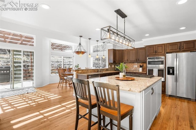 kitchen with tasteful backsplash, light wood-style flooring, appliances with stainless steel finishes, decorative light fixtures, and crown molding