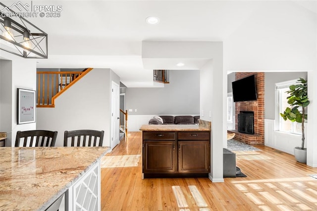 kitchen featuring light wood-style floors, a brick fireplace, light stone counters, and dark brown cabinets