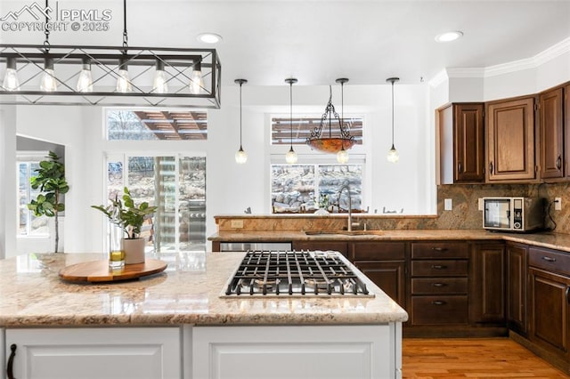 kitchen featuring light stone counters, stainless steel gas cooktop, a kitchen island, a sink, and decorative backsplash