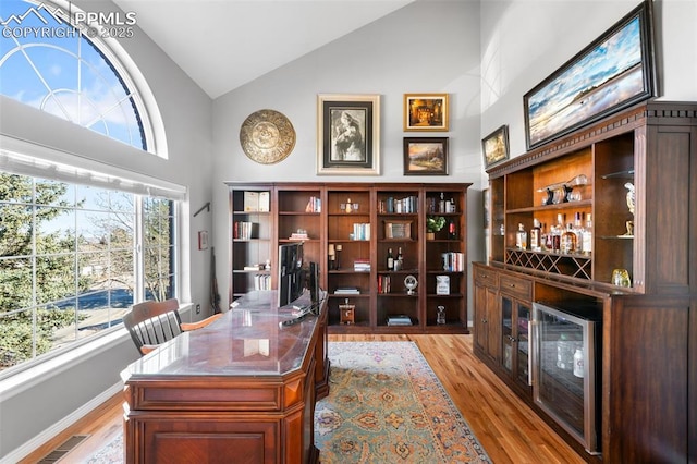 home office with a dry bar, visible vents, light wood-style flooring, high vaulted ceiling, and baseboards