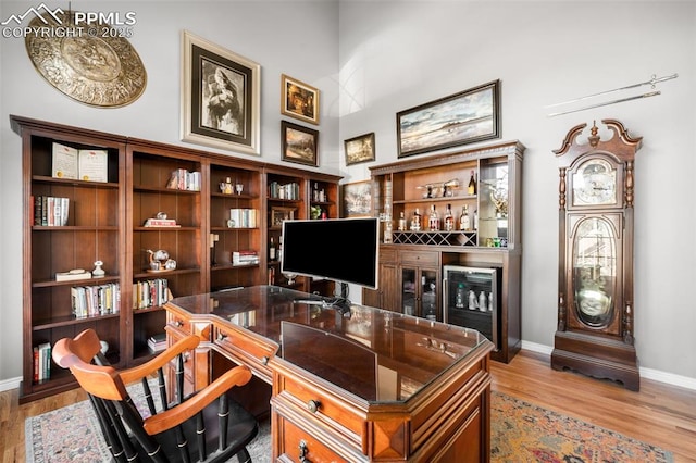 office space featuring light wood-type flooring, a high ceiling, baseboards, and a dry bar