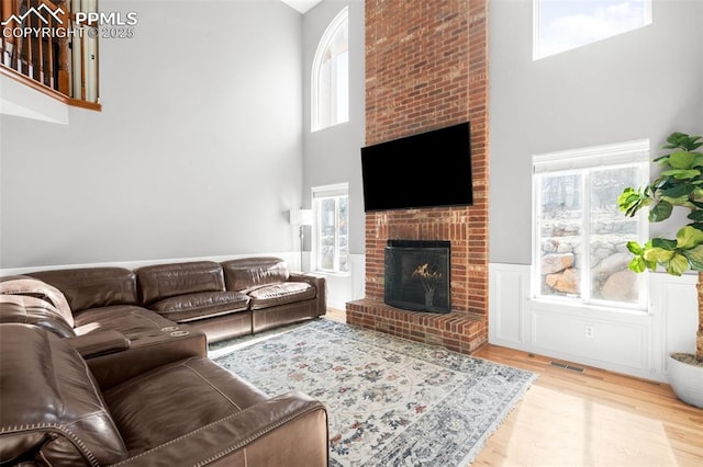 living room featuring visible vents, a fireplace, a towering ceiling, and wood finished floors