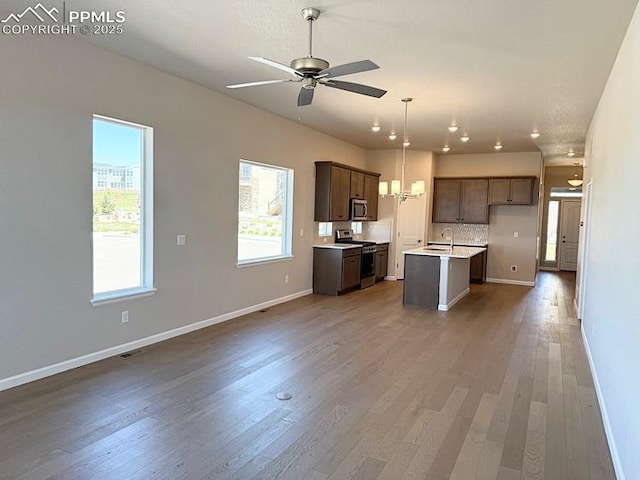 9463 Jollity Pt, Colorado Springs, CO 80924 - kitchen featuring appliances with stainless steel finishes, light countertops, open floor plan, a center island with sink, and ceiling fan with notable chandelier