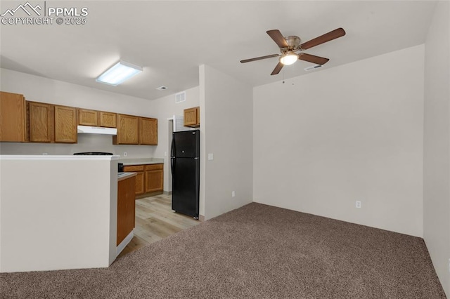 kitchen with visible vents, brown cabinets, light carpet, under cabinet range hood, and freestanding refrigerator