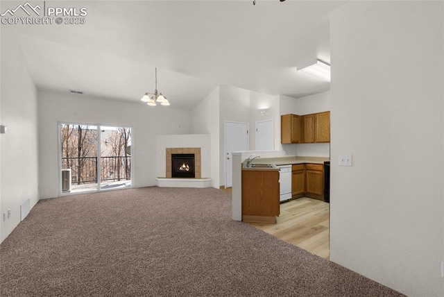 unfurnished living room with visible vents, light colored carpet, a tile fireplace, an inviting chandelier, and a sink