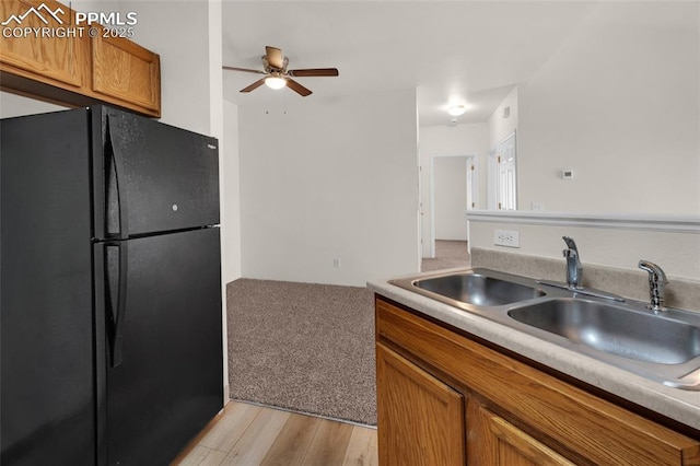 kitchen featuring light wood finished floors, light countertops, brown cabinets, freestanding refrigerator, and a sink