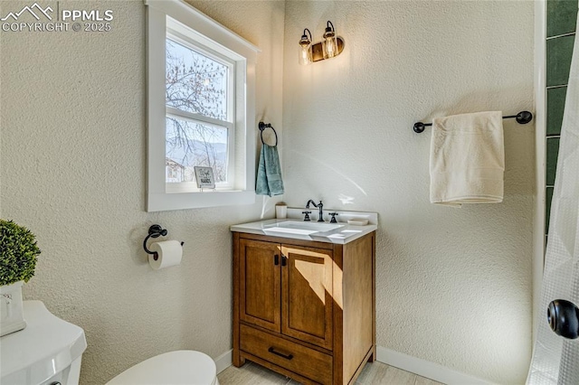 bathroom featuring baseboards, a textured wall, vanity, and toilet