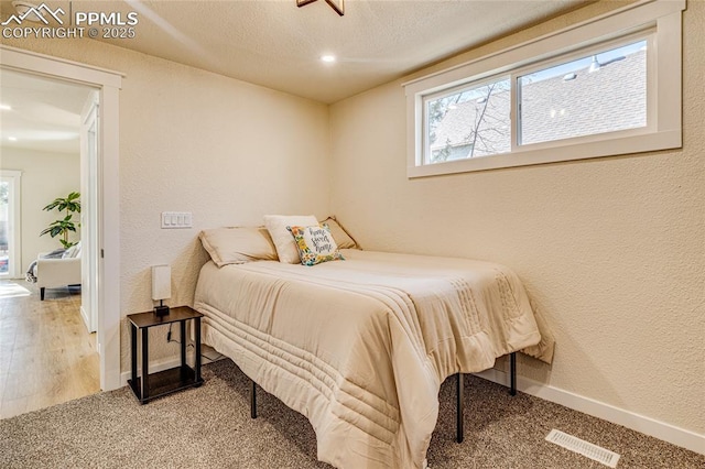 bedroom featuring baseboards, visible vents, a textured ceiling, and a textured wall