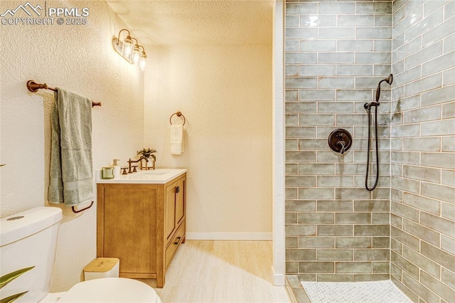 full bathroom with toilet, wood finished floors, vanity, baseboards, and tiled shower