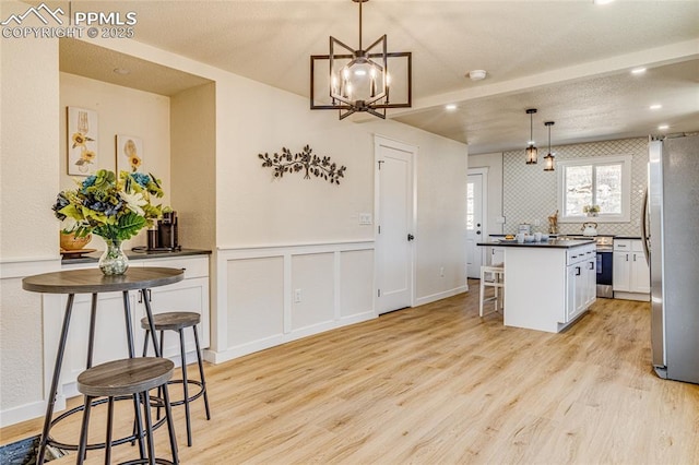 kitchen featuring dark countertops, freestanding refrigerator, white cabinetry, light wood-type flooring, and a kitchen breakfast bar