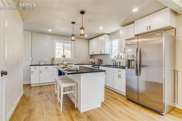 kitchen with dark countertops, white cabinetry, light wood finished floors, and stainless steel fridge with ice dispenser