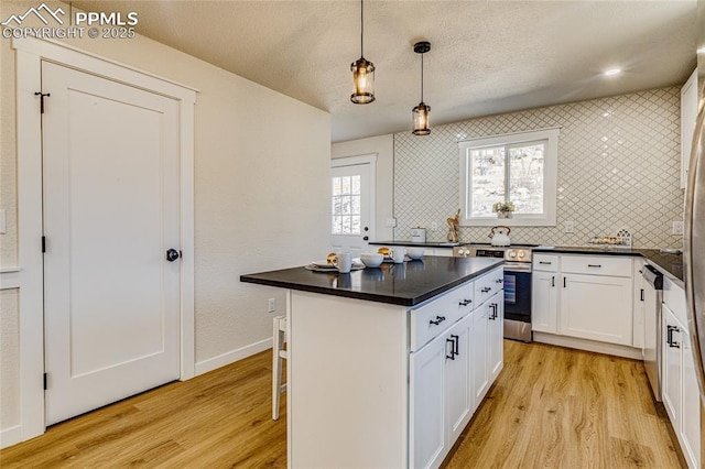 kitchen with white cabinets, light wood-style floors, appliances with stainless steel finishes, backsplash, and dark countertops