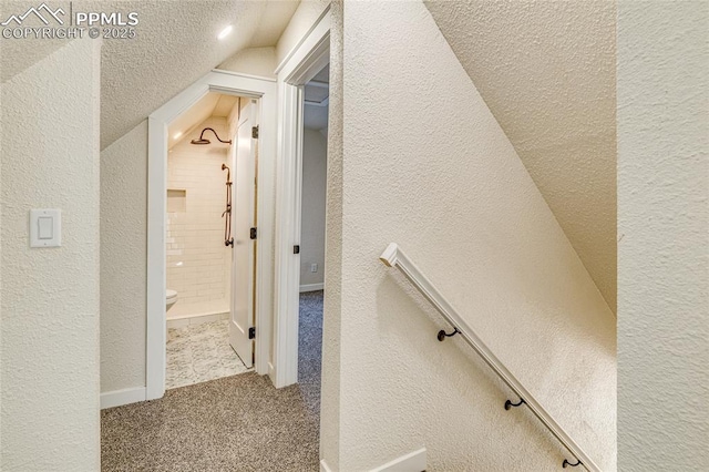 hall featuring vaulted ceiling, carpet flooring, a textured wall, and a textured ceiling