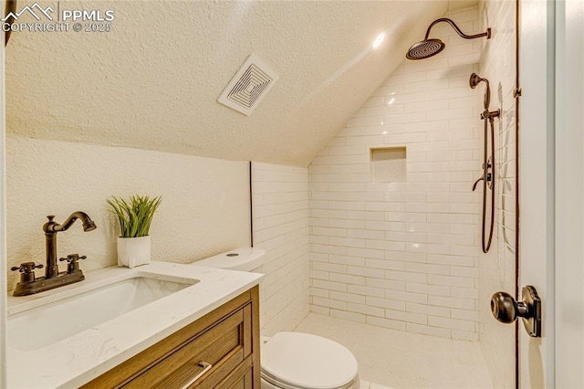 bathroom with lofted ceiling, visible vents, toilet, a tile shower, and a textured ceiling