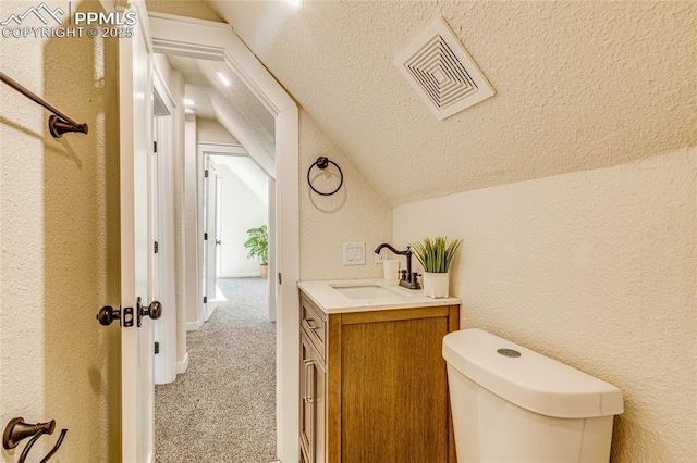 half bathroom featuring visible vents, a textured wall, lofted ceiling, a textured ceiling, and vanity