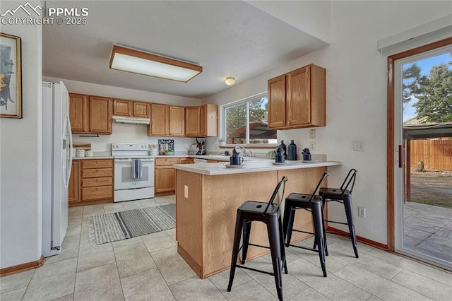 kitchen with light countertops, white appliances, a peninsula, baseboards, and under cabinet range hood