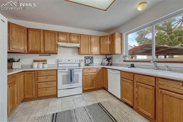 kitchen featuring white appliances, light countertops, a textured ceiling, under cabinet range hood, and a sink