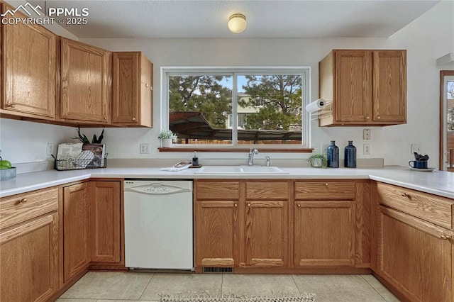 kitchen featuring brown cabinetry, light countertops, white dishwasher, and a sink