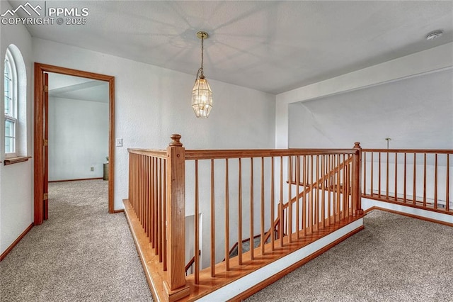 hall featuring an inviting chandelier, baseboards, carpet flooring, and an upstairs landing