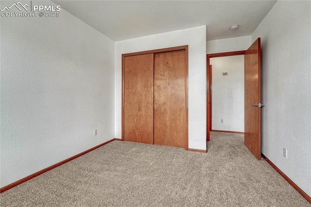 unfurnished bedroom featuring carpet floors, baseboards, a closet, and a textured wall