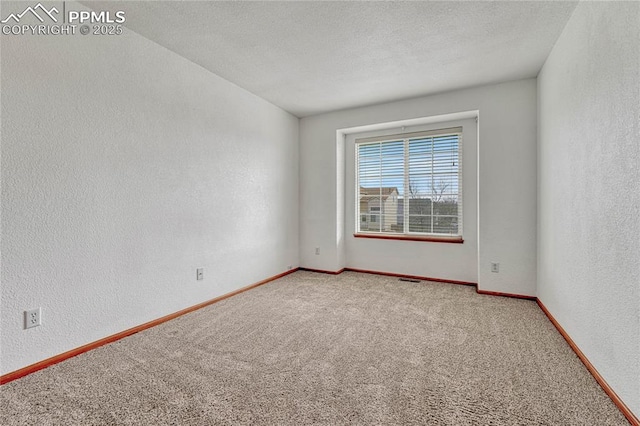 empty room with carpet flooring, a textured wall, a textured ceiling, and baseboards