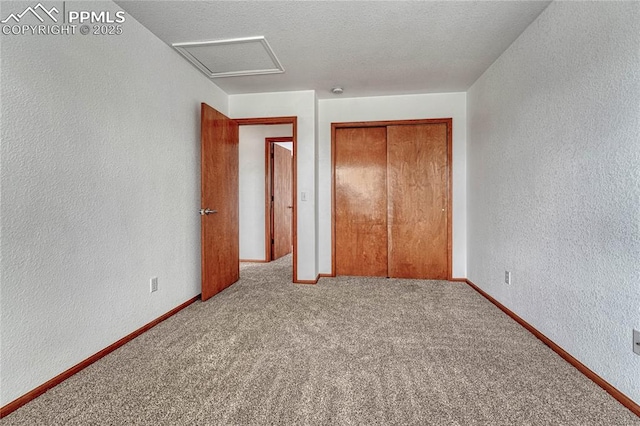 unfurnished bedroom featuring a textured wall, carpet, attic access, and baseboards