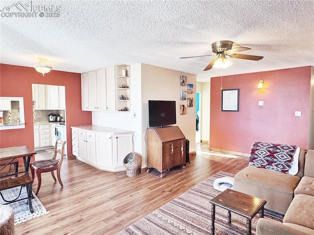 living area with ceiling fan, a textured ceiling, and light wood-style flooring