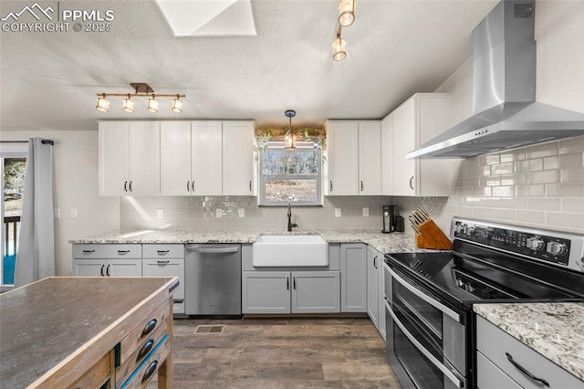 kitchen with a sink, stainless steel appliances, a wealth of natural light, and wall chimney exhaust hood