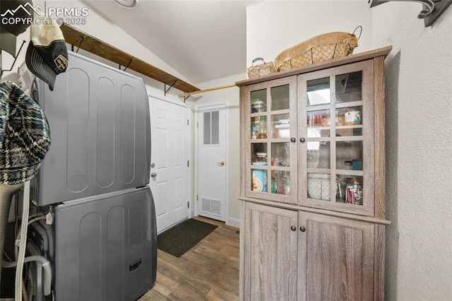 washroom featuring stacked washer / dryer, a textured ceiling, visible vents, and dark wood-style flooring
