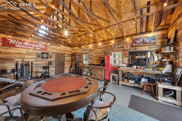 miscellaneous room featuring wooden walls, a workshop area, concrete flooring, and high vaulted ceiling