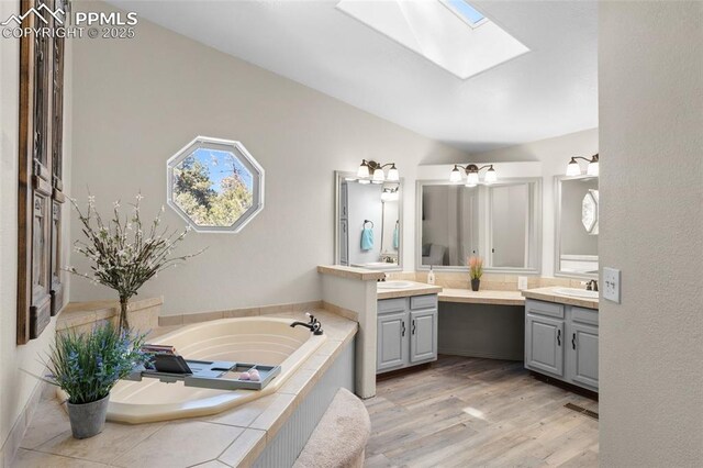 full bath featuring a skylight, wood finished floors, a garden tub, and two vanities