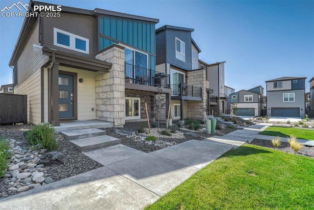 contemporary house with a balcony, stone siding, a residential view, and board and batten siding