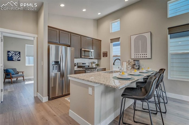 kitchen featuring light wood finished floors, stainless steel appliances, a sink, dark brown cabinets, and a kitchen breakfast bar