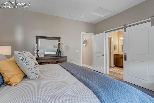 bedroom featuring ensuite bath, a barn door, and wood finished floors