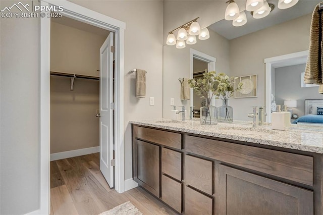 ensuite bathroom featuring double vanity, baseboards, a sink, and wood finished floors