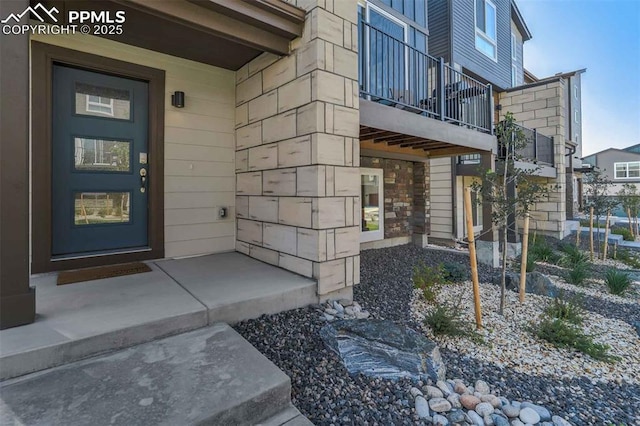 view of exterior entry with stone siding and a balcony