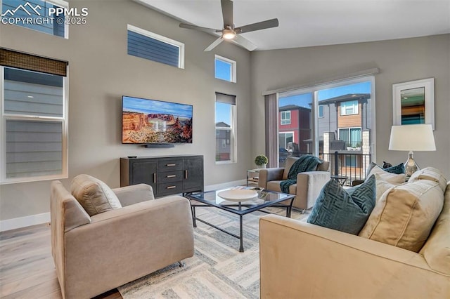 living area featuring light wood-style floors, ceiling fan, high vaulted ceiling, and baseboards