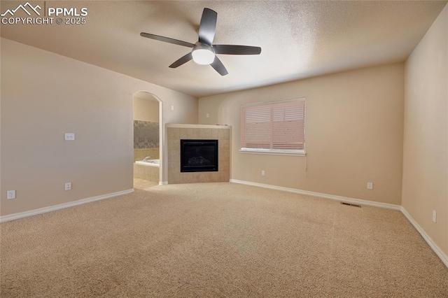 unfurnished living room with visible vents, baseboards, a ceiling fan, a tile fireplace, and carpet floors