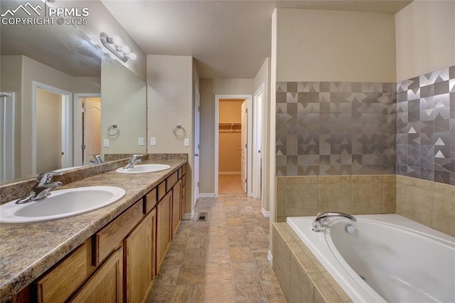 bathroom with a walk in closet, a garden tub, a sink, and double vanity