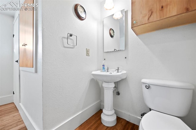 half bathroom featuring wood finished floors, toilet, and baseboards