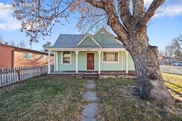 view of front facade with covered porch, a shingled roof, a front lawn, and fence