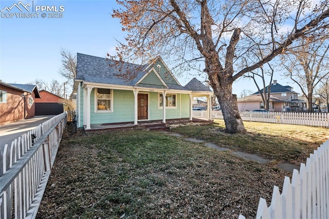 view of front facade featuring a porch, roof with shingles, a front yard, and a fenced backyard