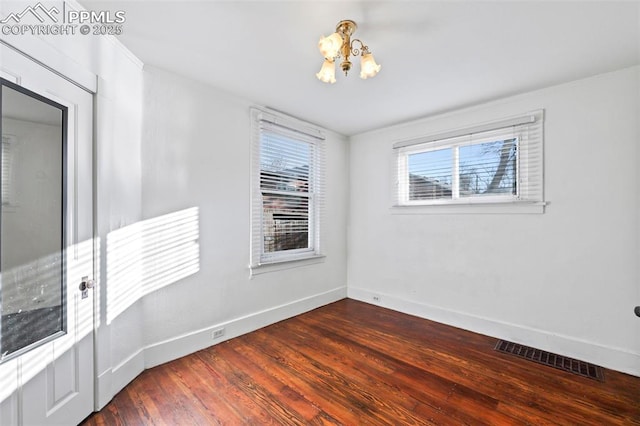 unfurnished room featuring a notable chandelier, wood finished floors, visible vents, and baseboards