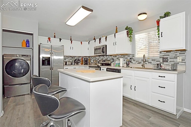 kitchen with appliances with stainless steel finishes, washer / clothes dryer, a sink, and light wood finished floors