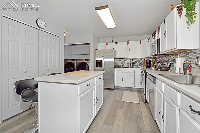 kitchen featuring a kitchen island, light wood-style floors, appliances with stainless steel finishes, backsplash, and washer and clothes dryer