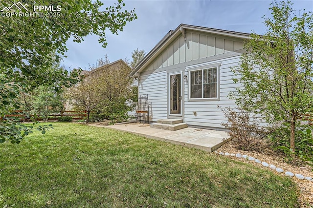 rear view of property featuring entry steps, a patio, fence, a yard, and board and batten siding