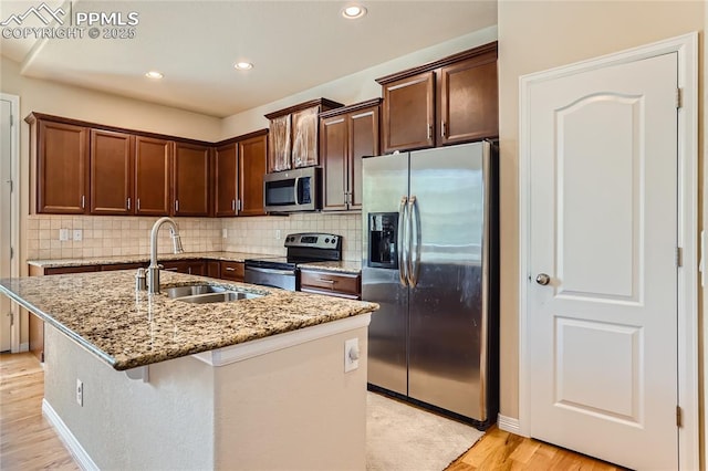 kitchen with light stone counters, light wood-style flooring, a sink, appliances with stainless steel finishes, and tasteful backsplash