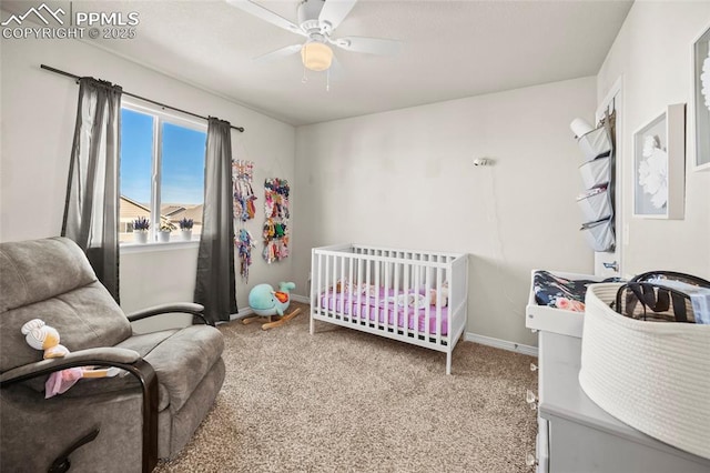 carpeted bedroom featuring a ceiling fan, a nursery area, and baseboards