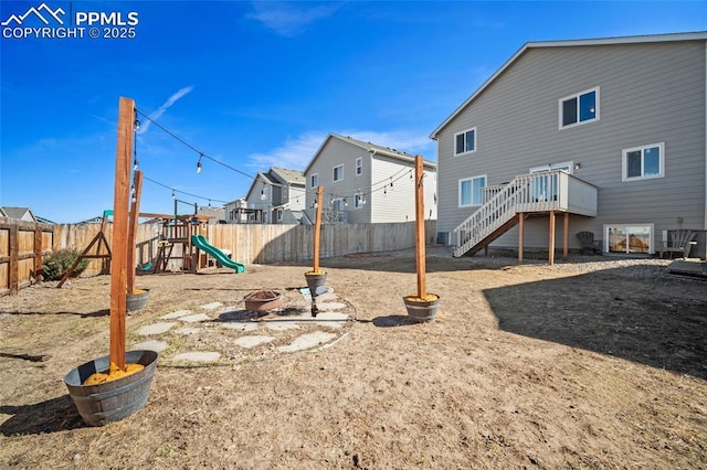 view of playground featuring stairs, a deck, a fire pit, and a fenced backyard