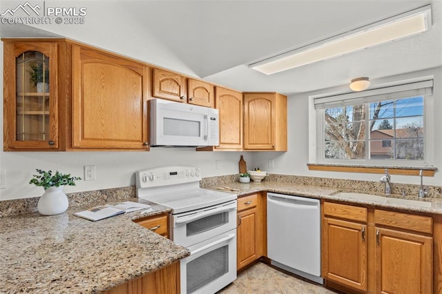 kitchen featuring glass insert cabinets, brown cabinetry, a sink, light stone countertops, and white appliances